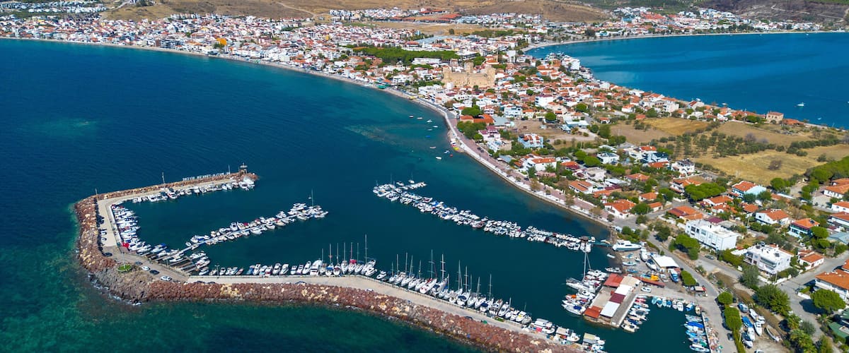 An aerial view of a coastal town with a marina, houses, and wind turbines in the background.