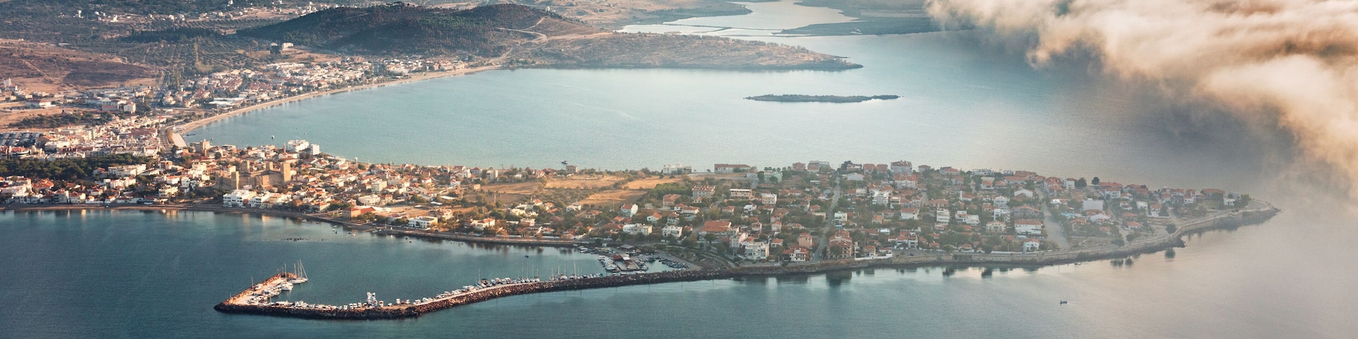 Vista aérea de una ciudad costera con una península destacada, un puerto deportivo y un puente que conecta la parte continental con la península.