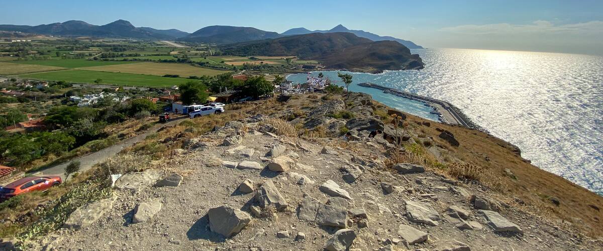 A coastal landscape with rocky terrain, a pier, and distant mountains.