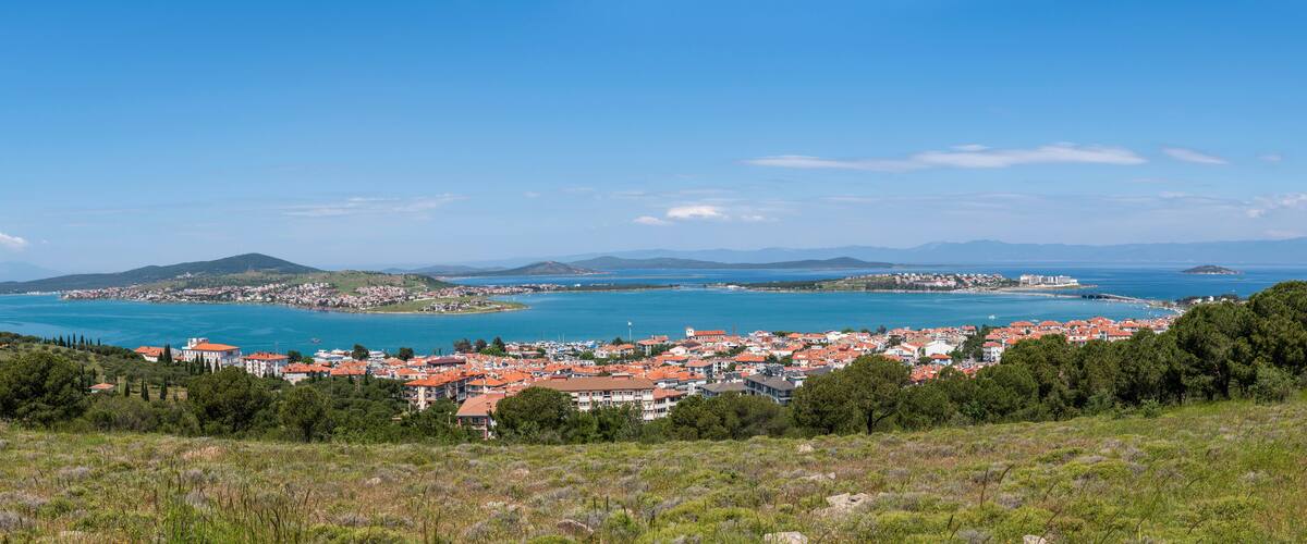 A coastal town with red-roofed buildings, a bay, and distant mountains.