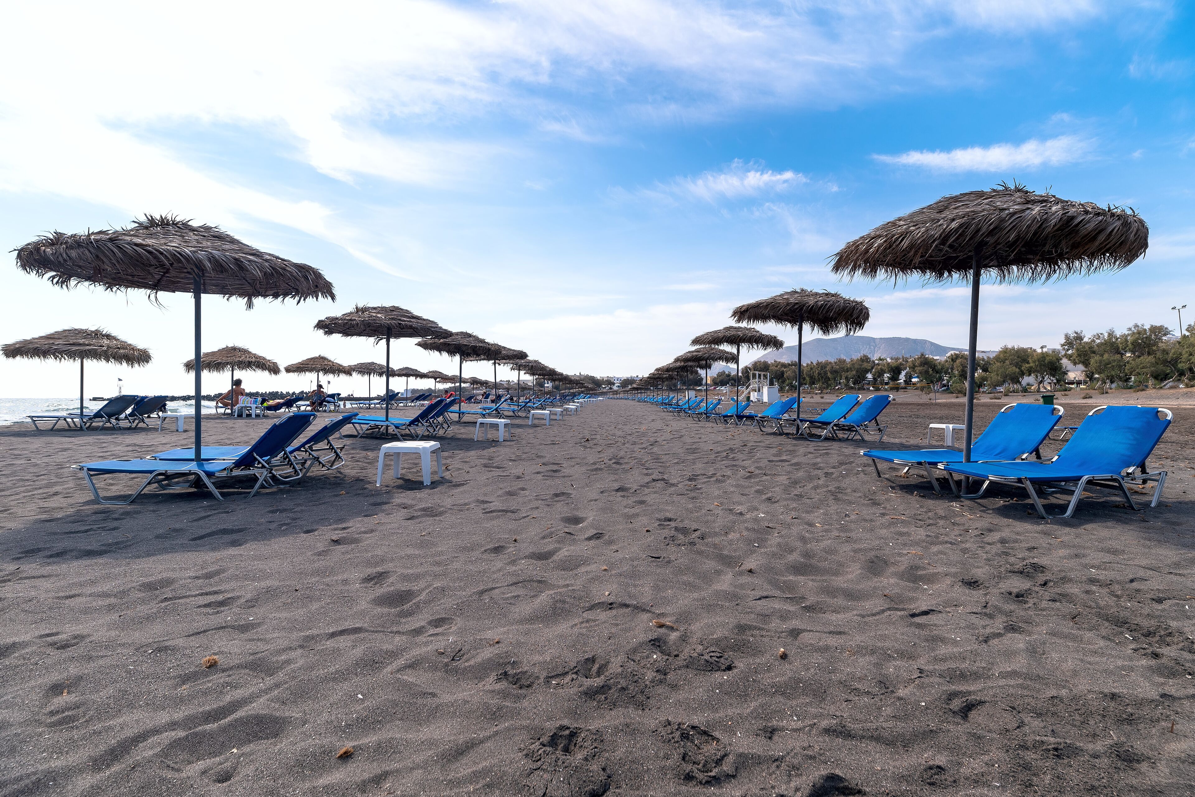 A beach with rows of blue lounge chairs and thatched umbrellas.