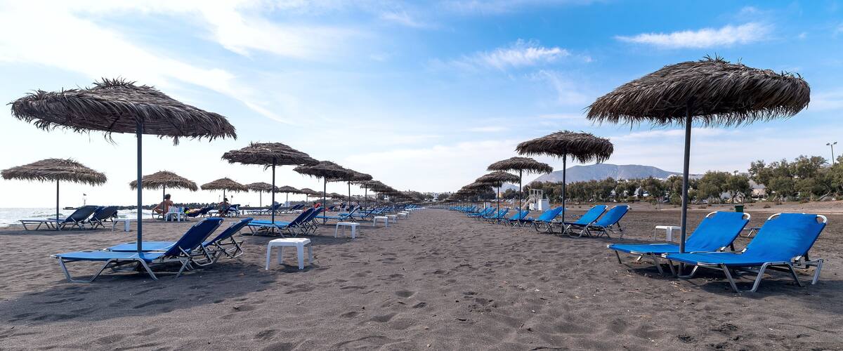 A beach with rows of blue lounge chairs and thatched umbrellas.