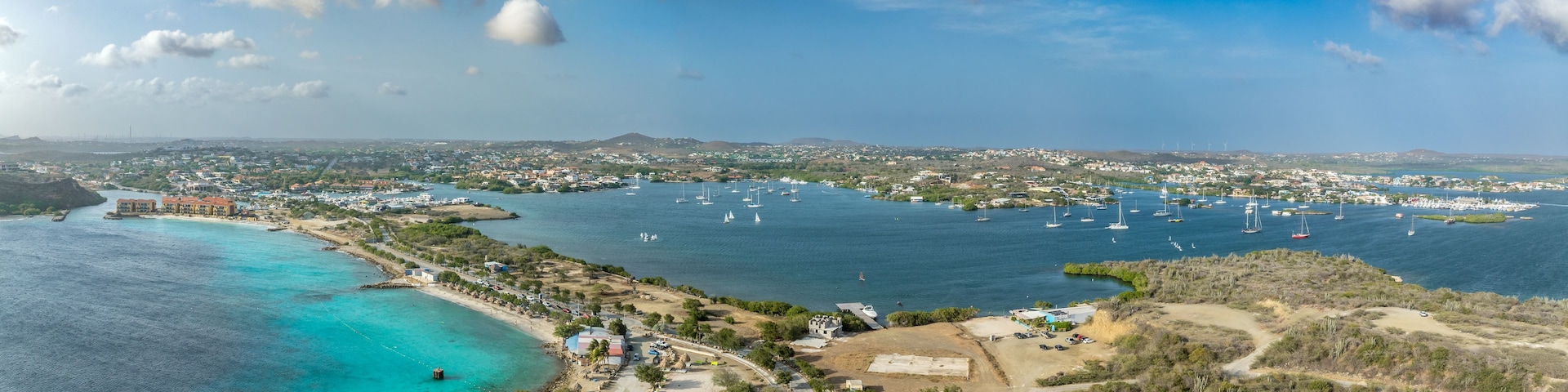 Un pueblo costero con un puerto deportivo, aguas turquesas cristalinas y un paisaje montañoso al fondo.