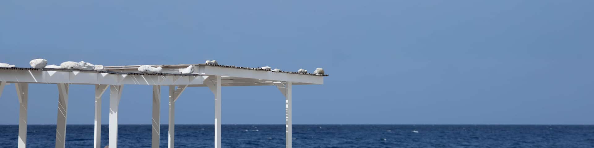 A white gazebo with a clear view of the ocean and a blue sky.