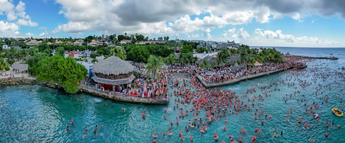 A crowded beach with people swimming and a thatched-roof structure.