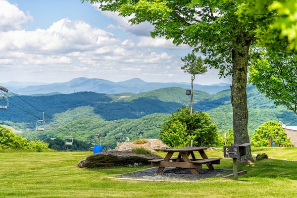 Sugar Mountain ski resort town park with idyllic picnic table bench under tree and view of ski chair slope and beautiful green North Carolina Blue Ridge Appalachia