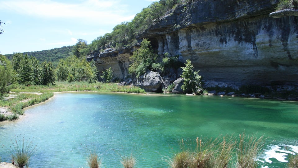 A clear turquoise lake surrounded by rocky cliffs and greenery.