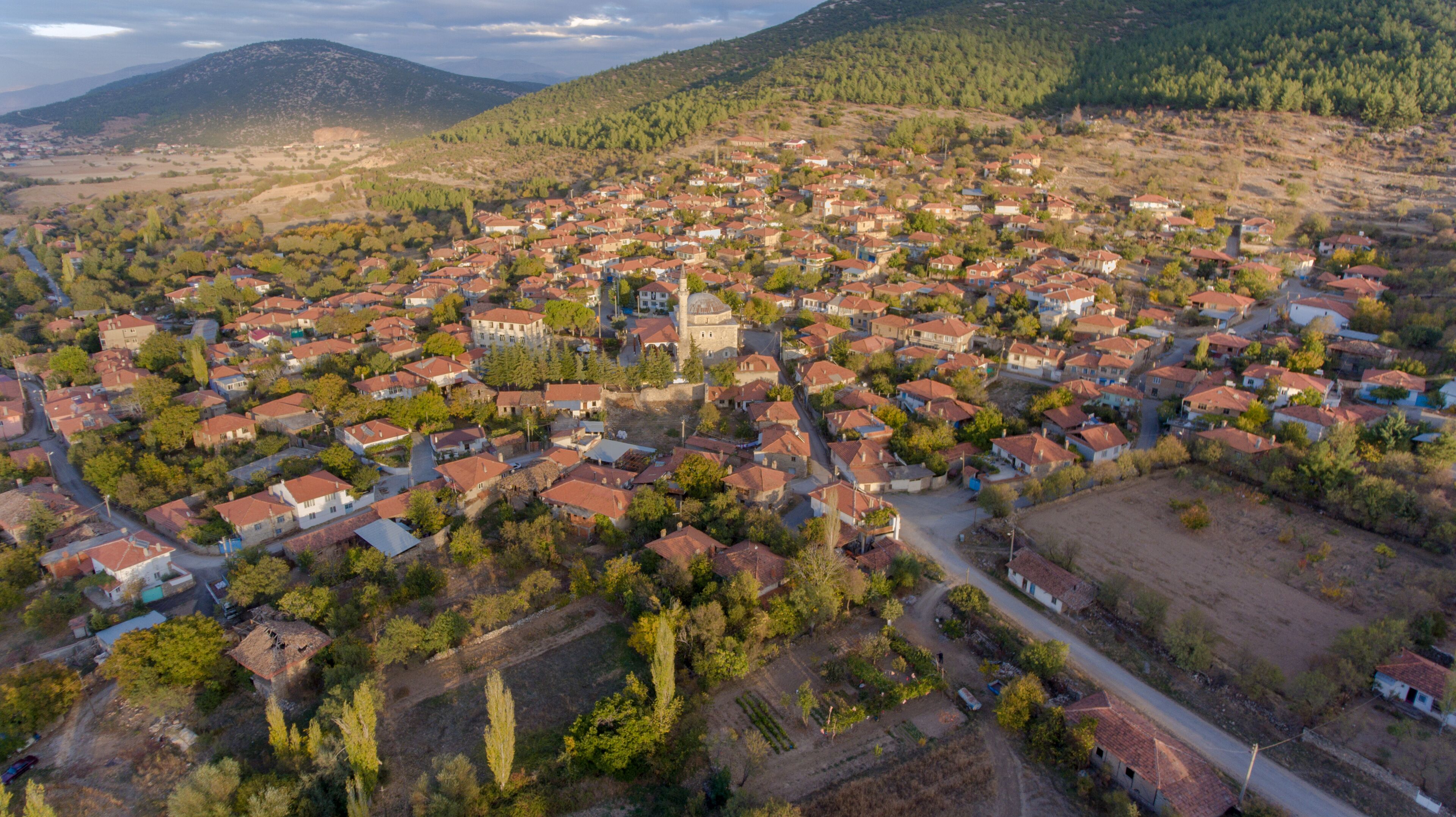 An aerial view of a town with red-roofed houses, a central church, and surrounding hills.