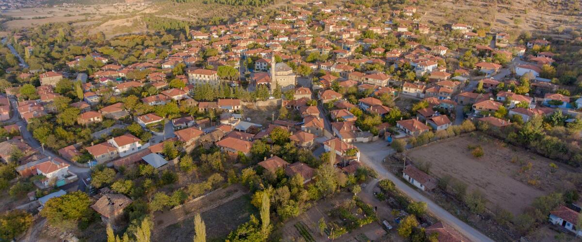 An aerial view of a town with red-roofed houses, a central church, and surrounding hills.