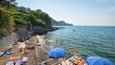 Une plage où des gens se prélassent au soleil et se baignent, entourée de verdure et de falaises rocheuses.