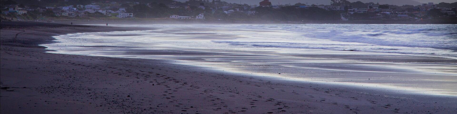 Une plage avec des vagues, une ville en arrière-plan et des montagnes.