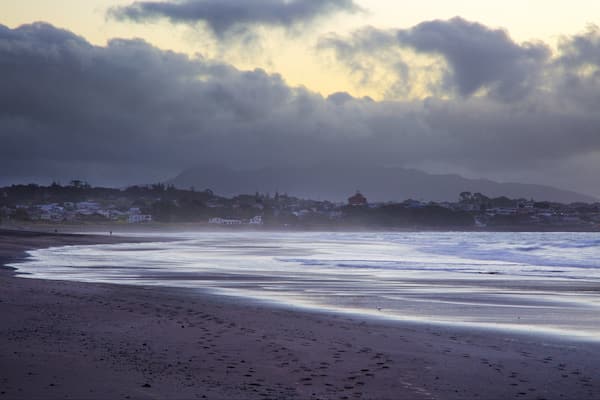Une plage avec des vagues, une ville en arrière-plan et des montagnes.