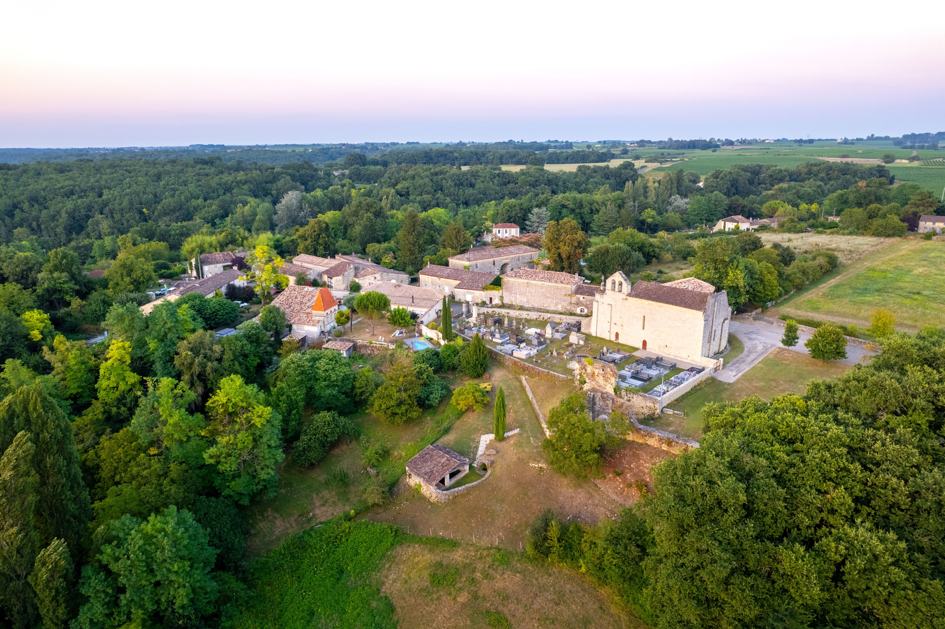An aerial view of a historic village with a prominent church, surrounded by dense forests and rolling fields.