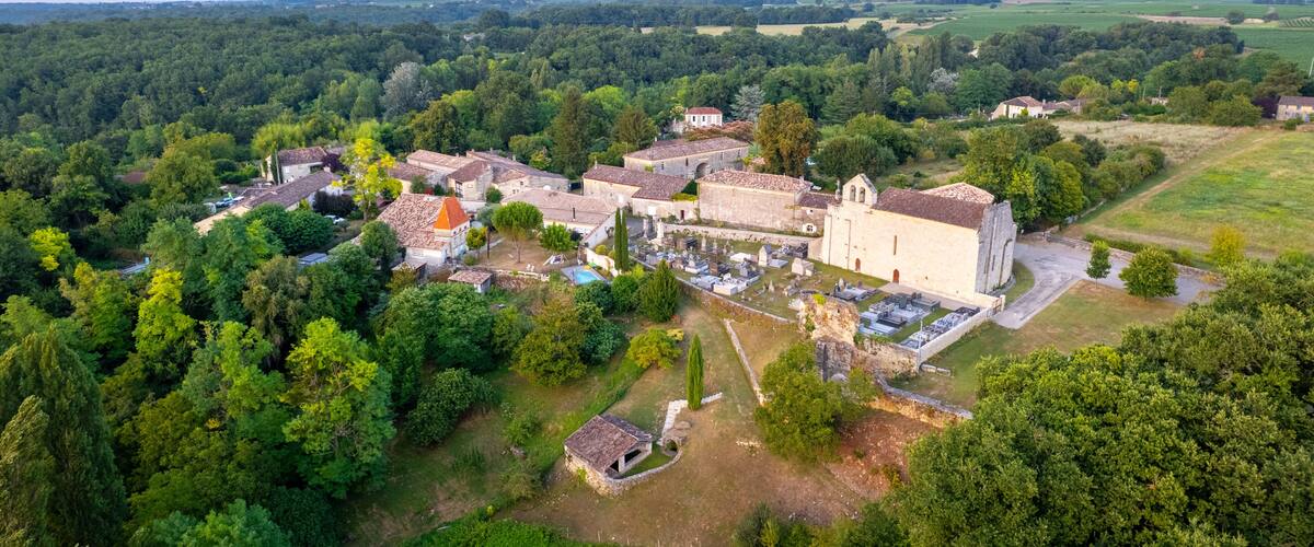 An aerial view of a historic village with a prominent church, surrounded by dense forests and rolling fields.