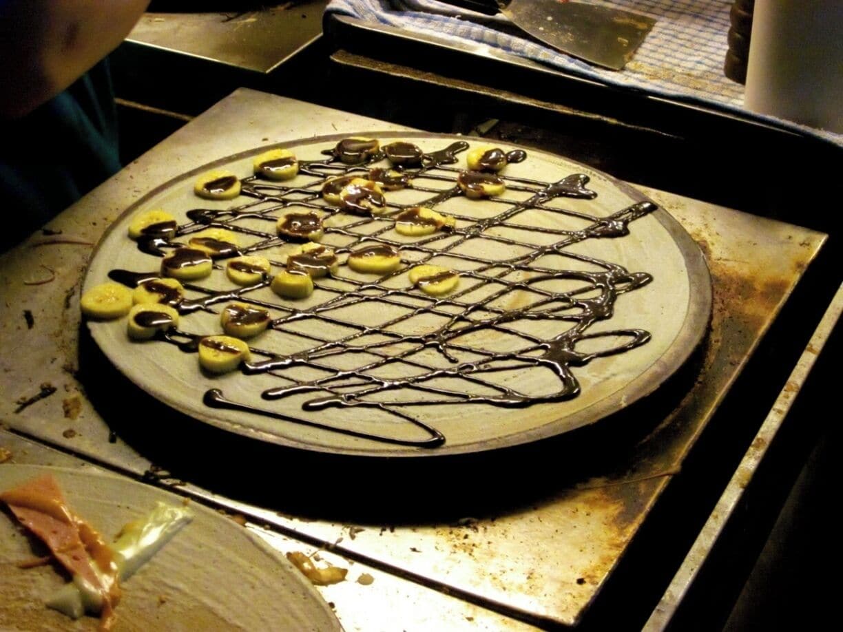 A pizza with toppings and chocolate drizzle on a metal tray.