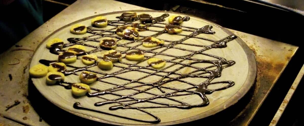 A pizza with toppings and chocolate drizzle on a metal tray.