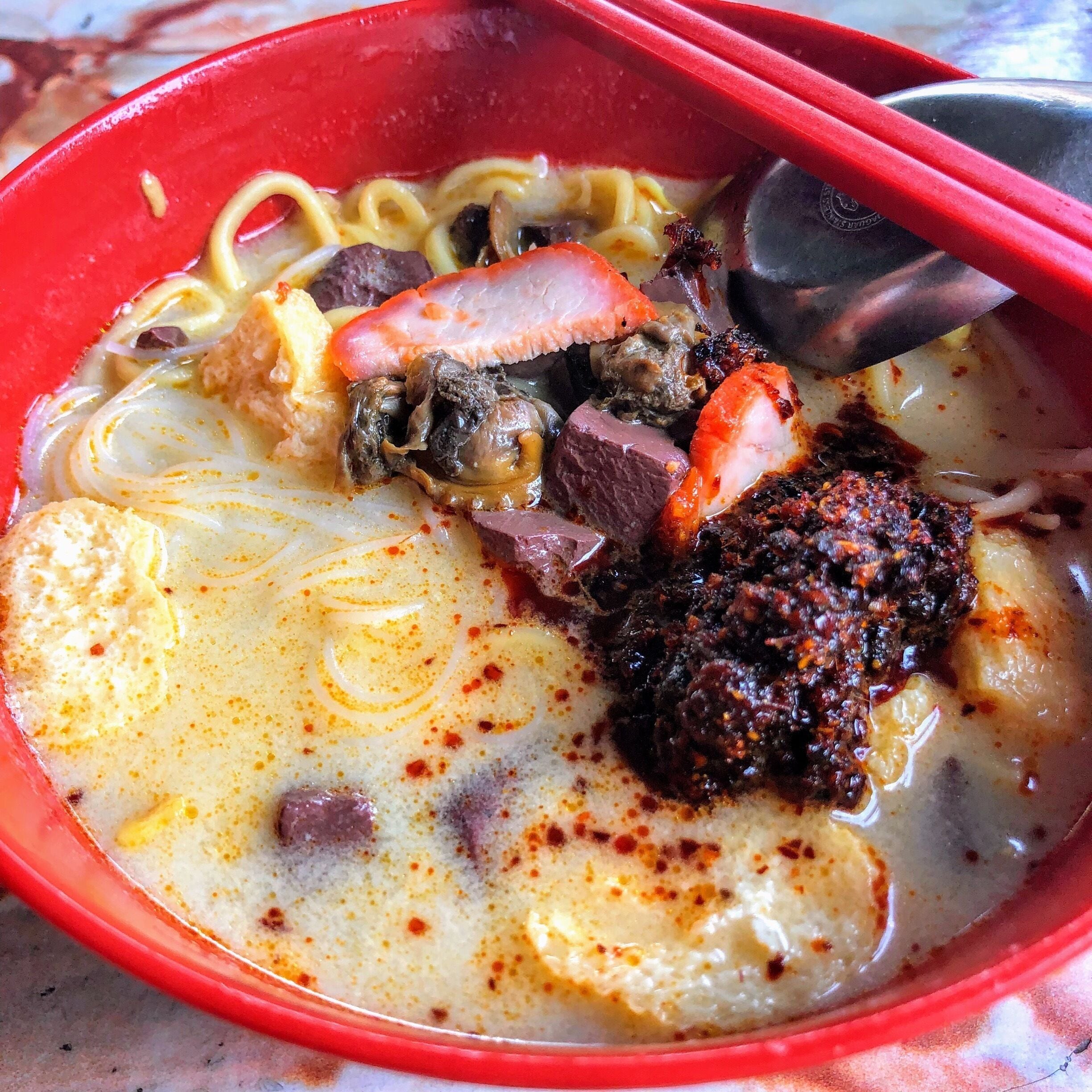 A bowl of ramen with noodles, meat, and a spicy topping.
