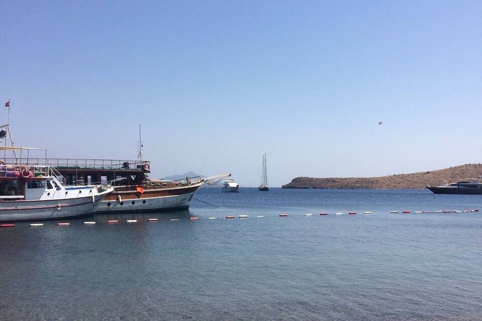 Un puerto tranquilo con barcos amarrados, cielo despejado y un puente a lo lejos.