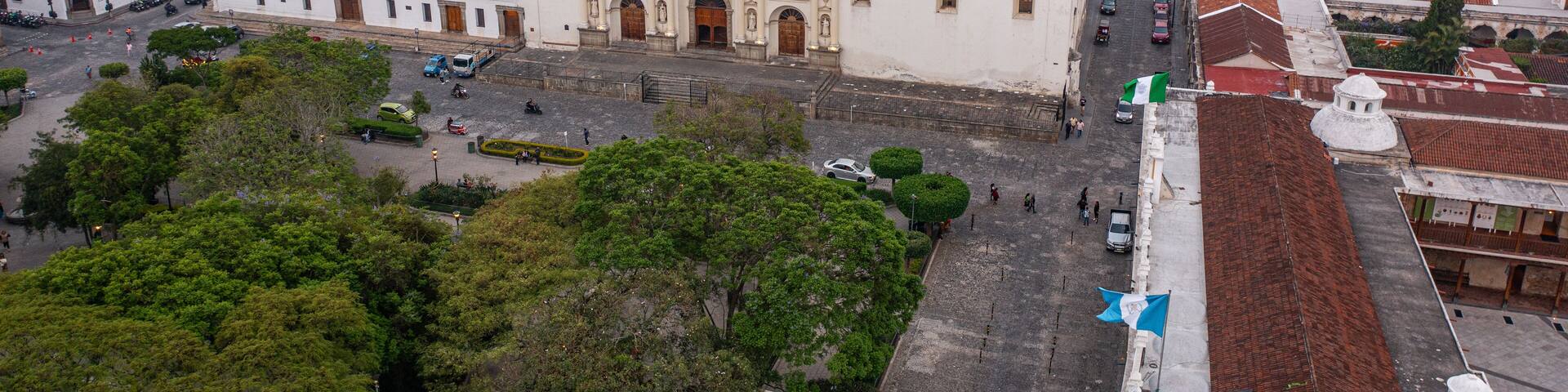 Templo iglesia del Santo Hermano Pedro de Antigua Guatemala fachada vieja antigua con plaza central con muchos árboles con calles alrededor con casas y edificios al fondo