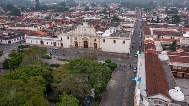 Templo iglesia del Santo Hermano Pedro de Antigua Guatemala fachada vieja antigua con plaza central con muchos árboles con calles alrededor con casas y edificios al fondo