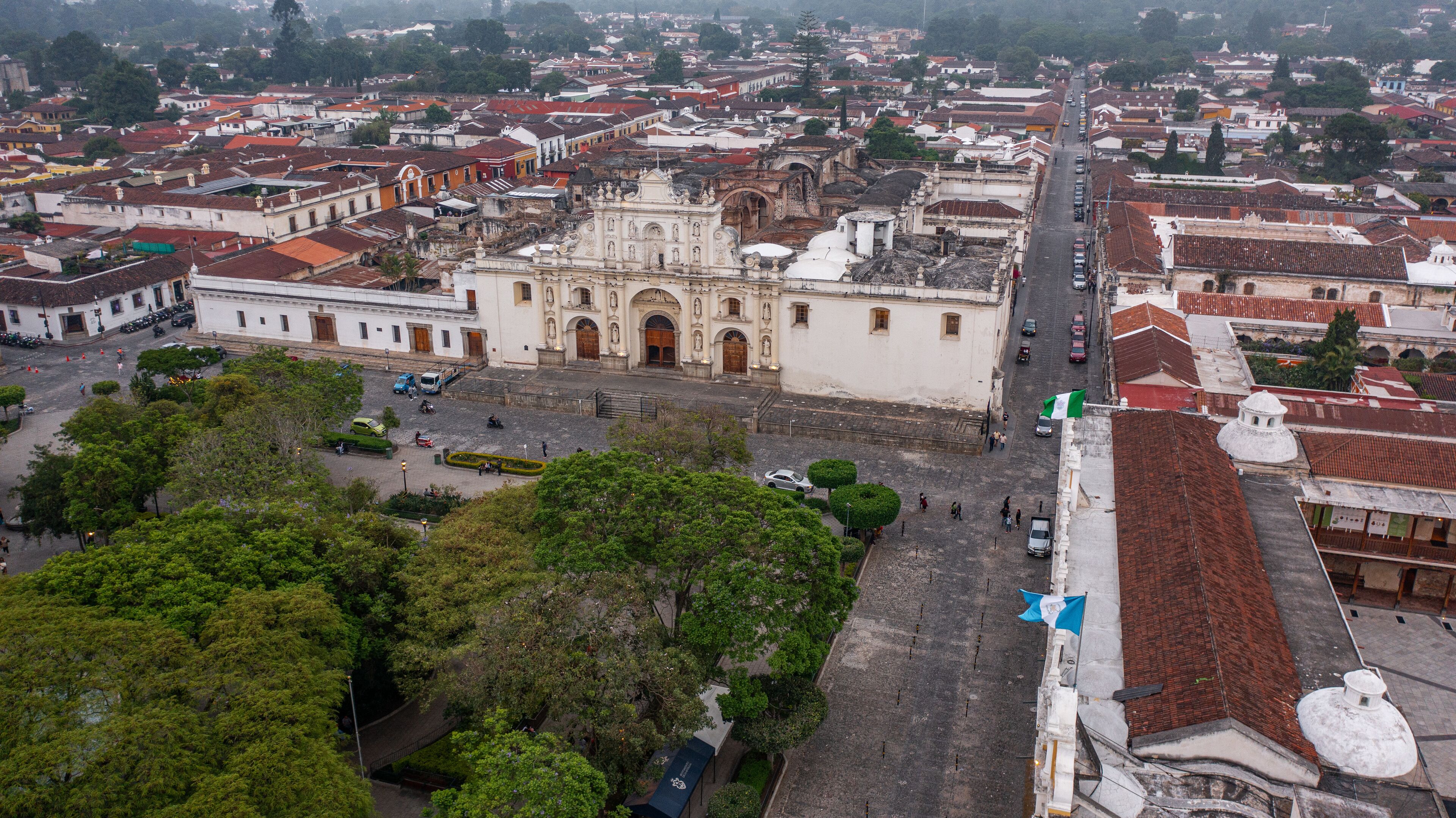 An aerial view of a historic city center with a prominent cathedral, narrow streets, and surrounding greenery.
