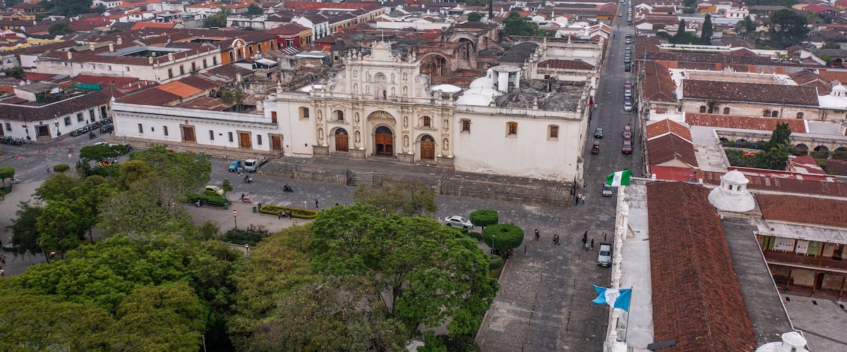 An aerial view of a historic city center with a prominent cathedral, narrow streets, and surrounding greenery.