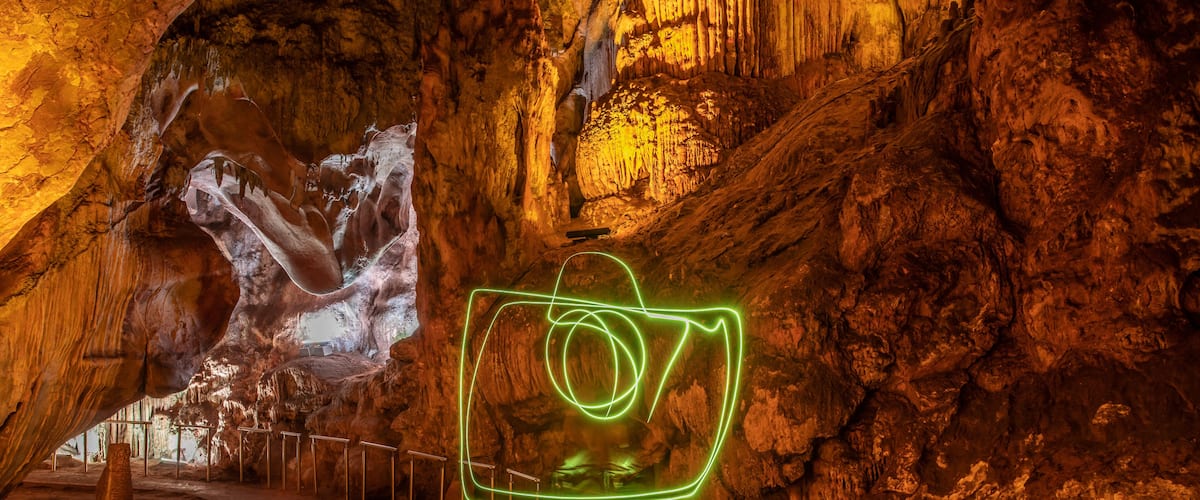 A cave with a green neon light installation and a large rock formation.