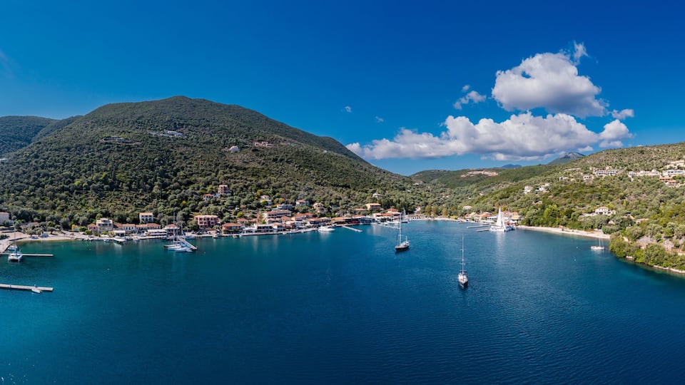 A coastal town with a marina, boats, and a mountainous backdrop.
