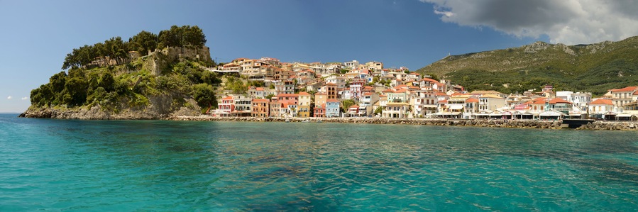 Un pueblo costero con edificios de colores en una colina, con vistas a aguas turquesas.