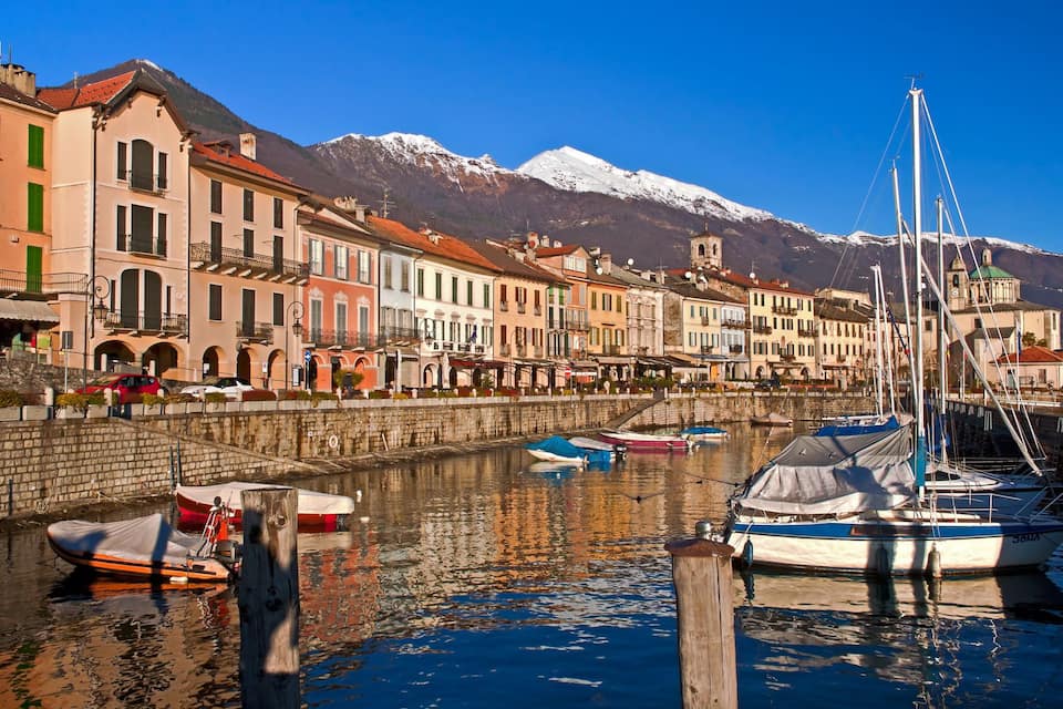 A harbor with colorful buildings, boats, and snow-capped mountains in the background.