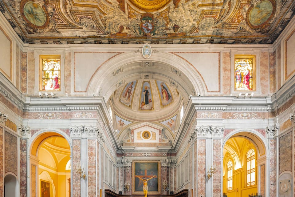 An ornate church interior with frescoes, stained glass windows, and a crucifix.