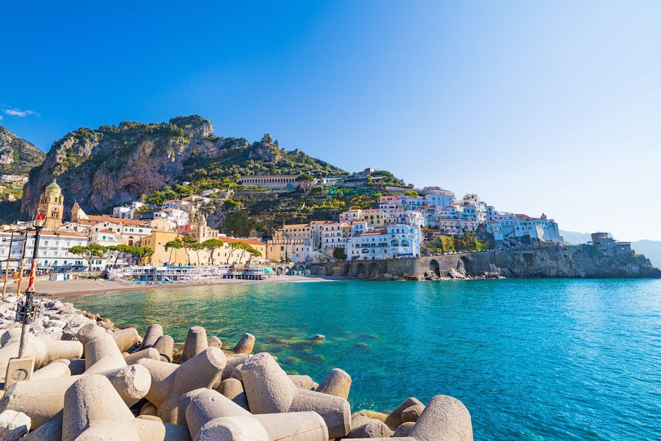 A coastal town with colorful buildings, a prominent church, and a rocky shoreline with large boulders.