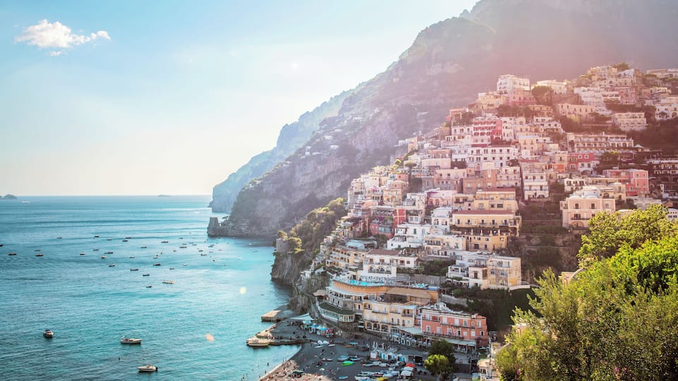 Positano's colourful villas stacked vertically up the side of the cliff with leisure and fishing boats on the ocean.