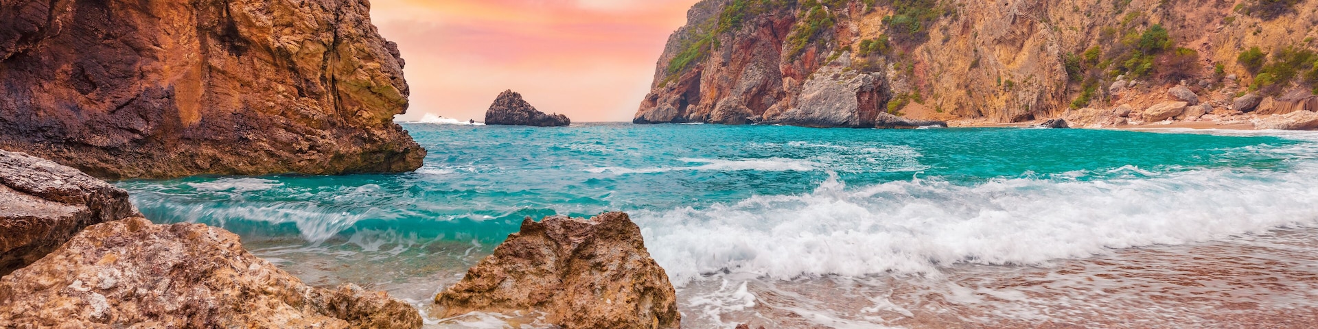 A rocky coastline with clear turquoise waters, a pebbled beach, and a dramatic cliff face.