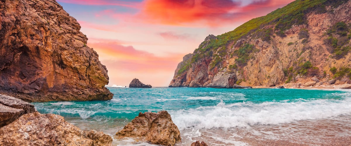 A rocky coastline with clear turquoise waters, a pebbled beach, and a dramatic cliff face.