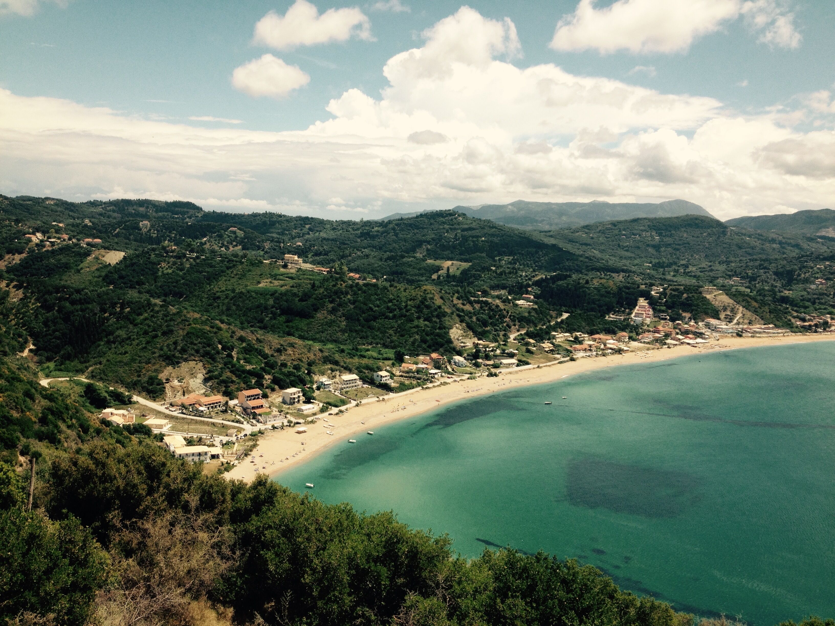 A coastal town with a beach, surrounded by hills and greenery.