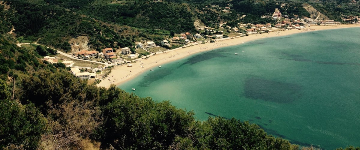 A coastal town with a beach, surrounded by hills and greenery.