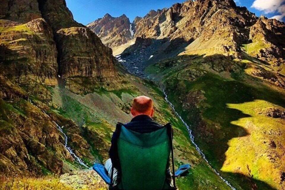 A person in a green chair overlooking a mountainous valley with a river.