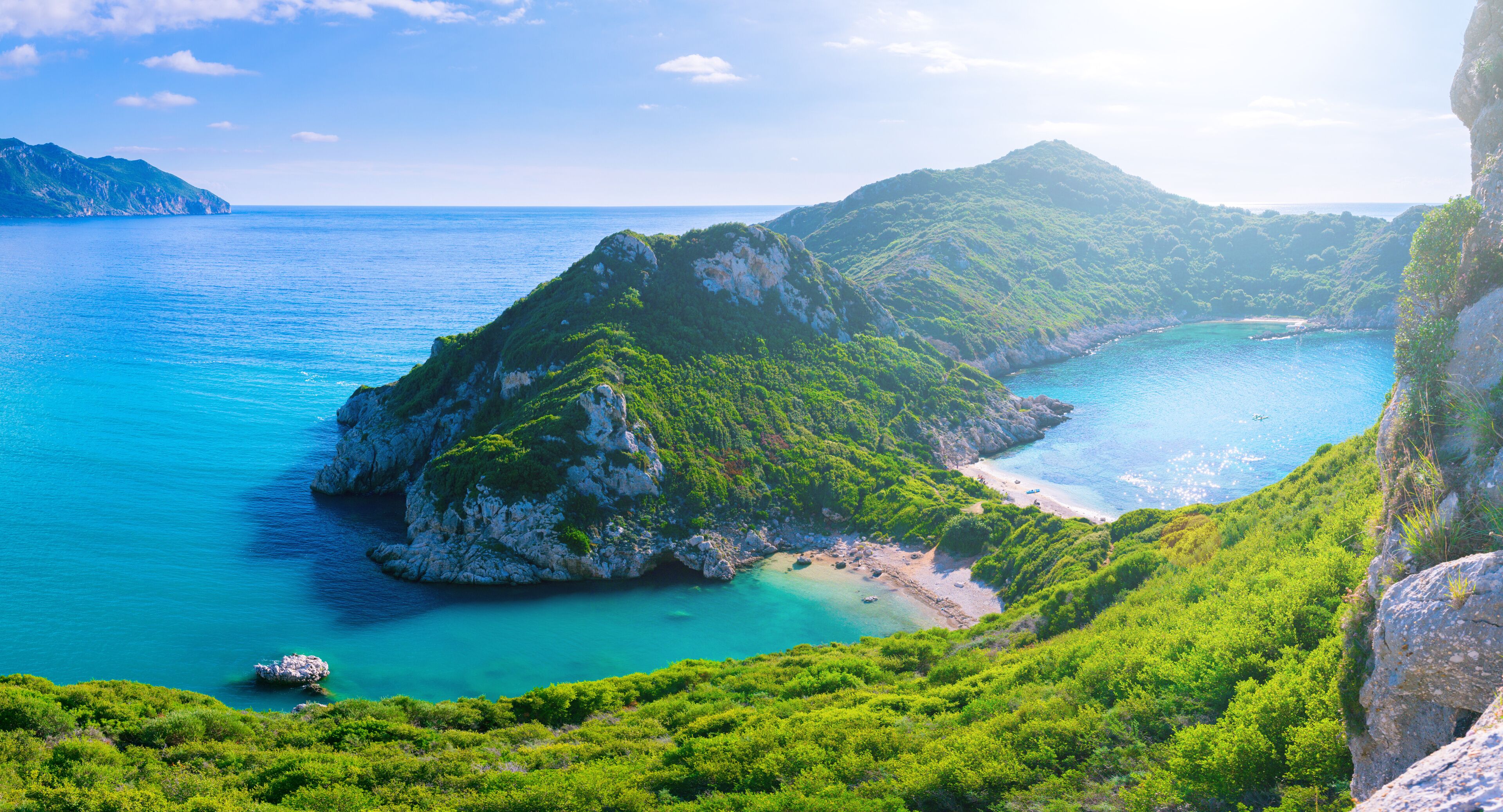 A coastal landscape with a prominent green hill, a clear blue sea, and a rocky shoreline.
