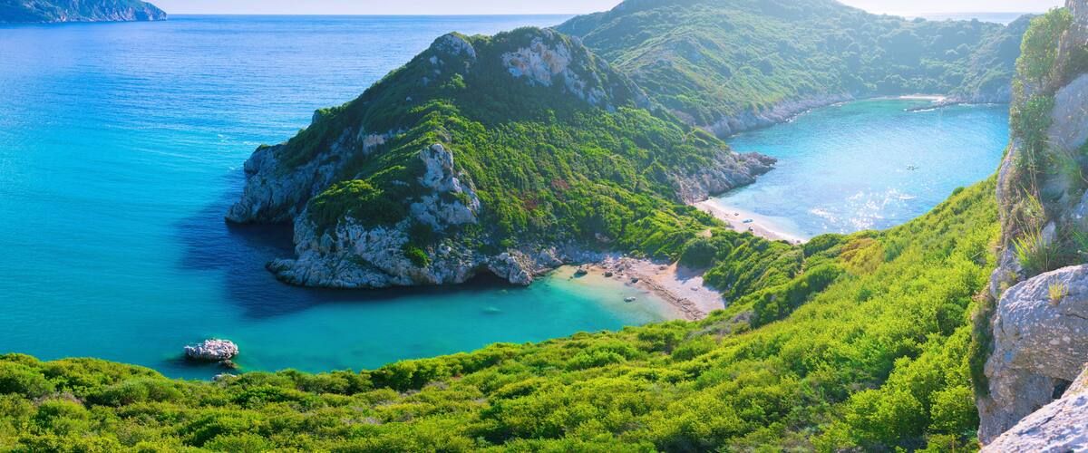 A coastal landscape with a prominent green hill, a clear blue sea, and a rocky shoreline.