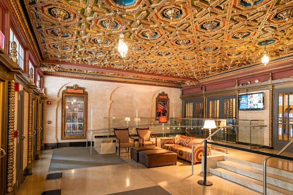 Ein aufwendig ausgestattetes Theaterinneres mit detailreicher Decke, komfortablen Sitzen und einer Treppe.