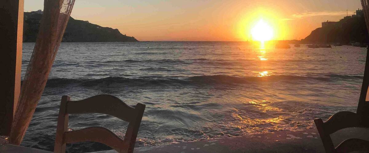 A sunset over the sea with chairs facing the view.