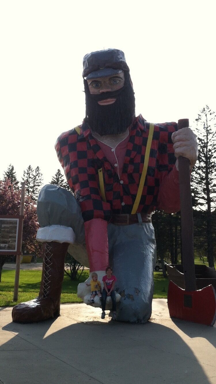 A large statue of a man in a checkered shirt and jeans holding a red axe.