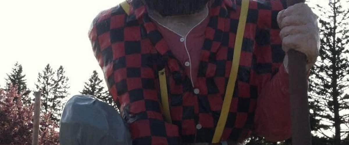 A large statue of a man in a checkered shirt and jeans holding a red axe.