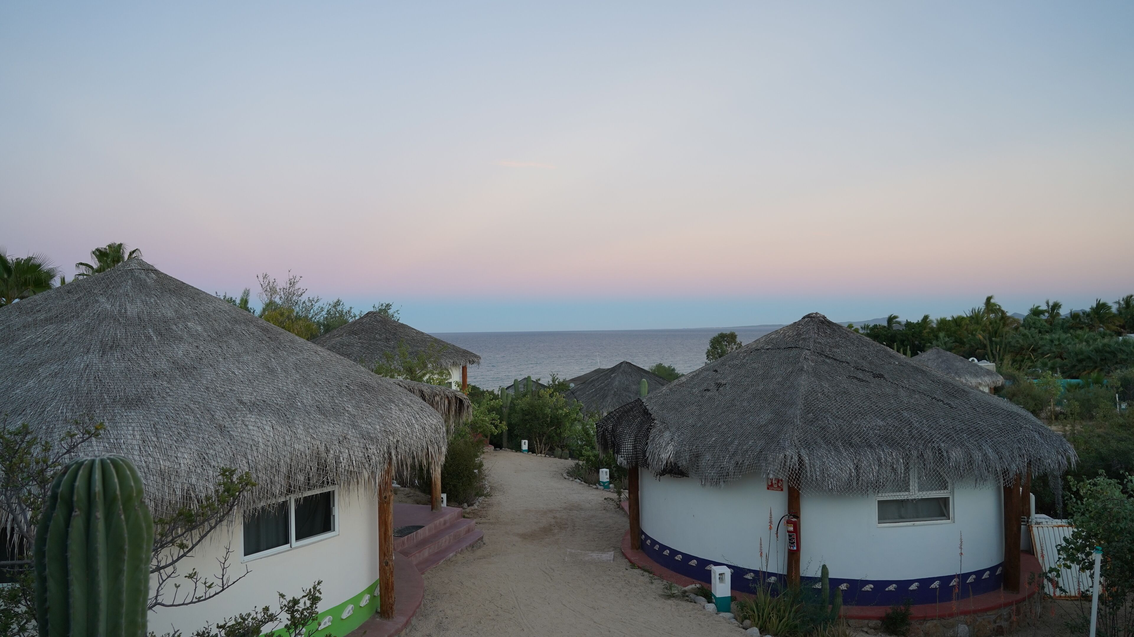 A coastal village with thatched-roof huts and a sandy path leading to the sea.