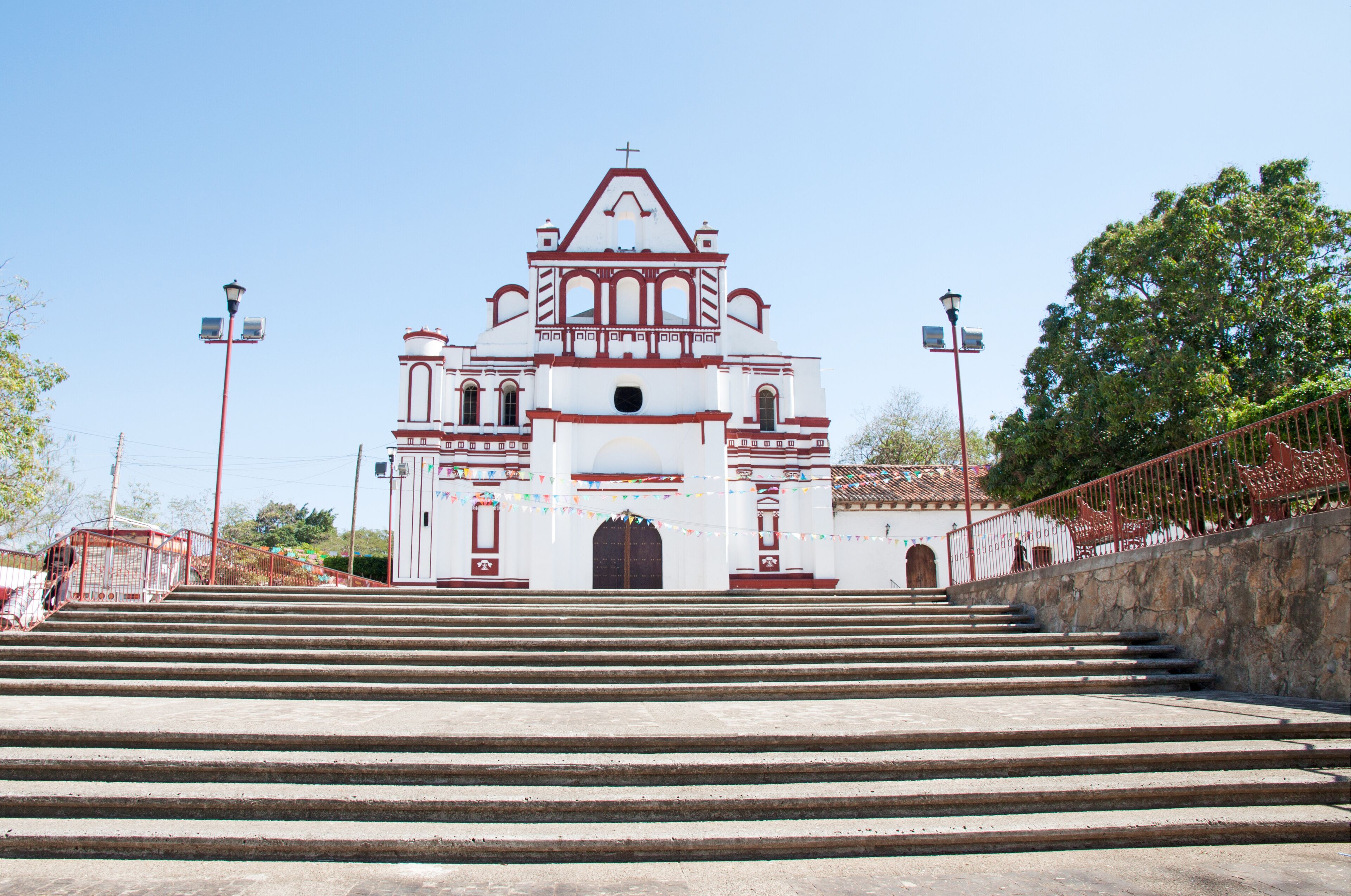 A white church with red trim and a bell tower, surrounded by steps and a stone wall.