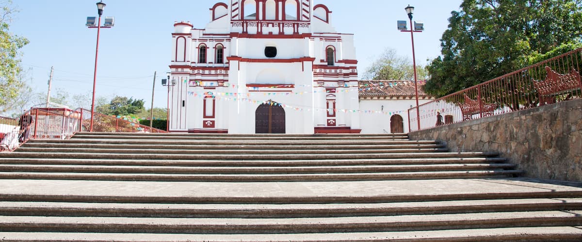 A white church with red trim and a bell tower, surrounded by steps and a stone wall.