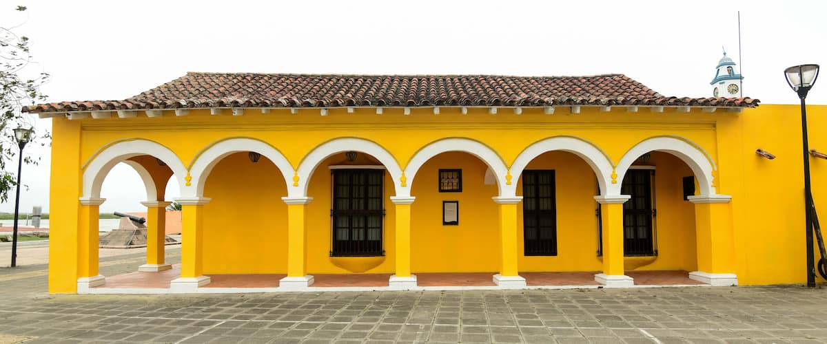 A yellow building with a tiled roof and white arches.