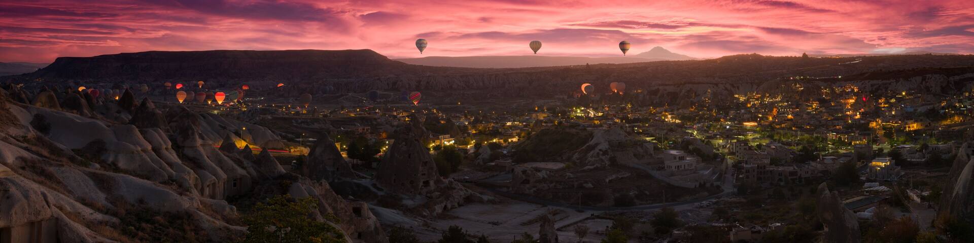 A cityscape at dusk with hot air balloons and a mountainous backdrop.