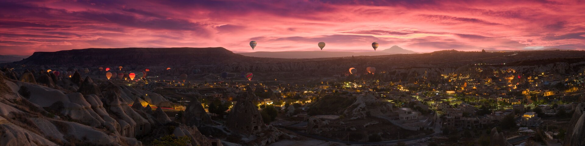 A cityscape at dusk with hot air balloons and a mountainous backdrop.
